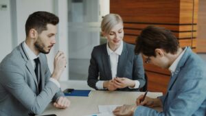 A legal/financial advisor reviewing paperwork with two clients in a modern office